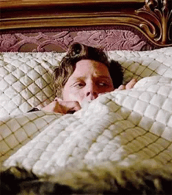 A Man Is Sticking His Head Out Of A Bed . GIF