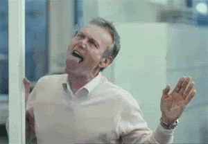 A Man Is Sticking His Tongue Out While Looking Out A Window . GIF