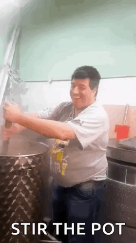 A Man Is Stirring A Pot In A Kitchen While Smiling . GIF