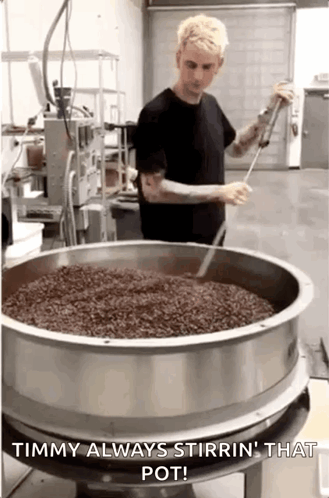 A Man Is Stirring A Pot Of Coffee Beans In A Kitchen . GIF