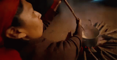 A Man Is Stirring A Pot Of Soup With A Wooden Ladle . GIF