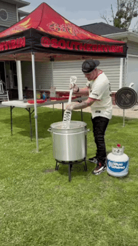 A Man Is Stirring Something In A Pot Under A Tent That Says Southern On It GIF