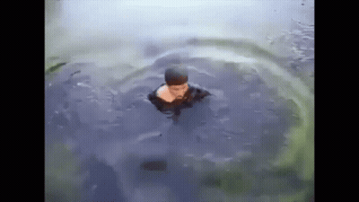 A Man Is Swimming In A Body Of Water With A Turtle Behind Him . GIF
