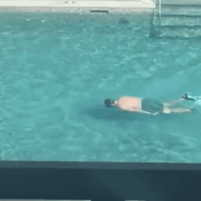 A Man Is Swimming In A Swimming Pool While Another Man Watches . GIF