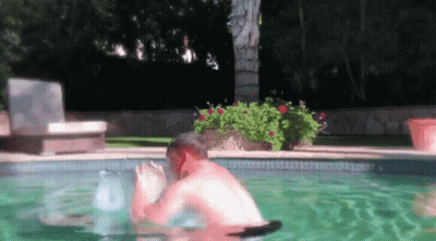 A Man Is Swimming In A Swimming Pool With A Chair In The Background . GIF