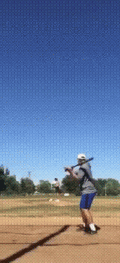 A Man Is Swinging A Bat At A Ball In A Field GIF