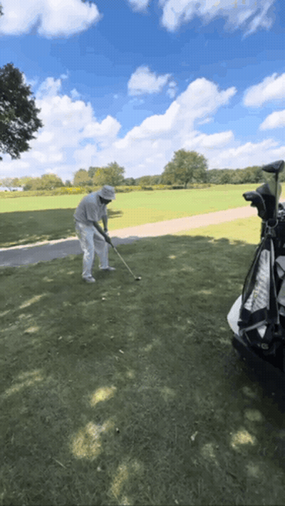 A Man Is Swinging A Golf Club At A Golf Ball GIF