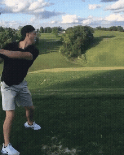 A Man Is Swinging A Golf Club At A Golf Ball GIF