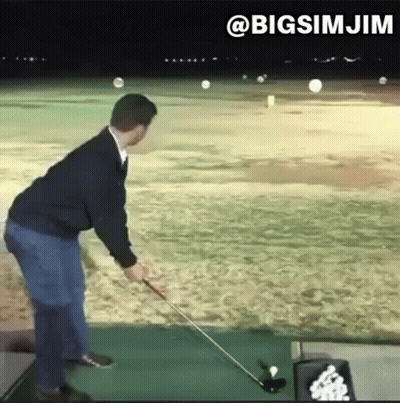 A Man Is Swinging A Golf Club At A Golf Ball On A Golf Course . GIF