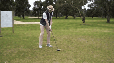 A Man Is Swinging A Golf Club At A Golf Ball On A Golf Course GIF