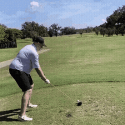 A Man Is Swinging A Golf Club At A Golf Ball On A Golf Course GIF