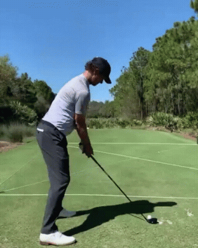 A Man Is Swinging A Golf Club At A Golf Ball On A Green . GIF