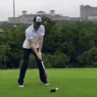 A Man Is Swinging A Golf Club At A Golf Ball . GIF