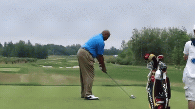 A Man Is Swinging A Golf Club On A Golf Course Next To A Bag That Says Taylormade GIF