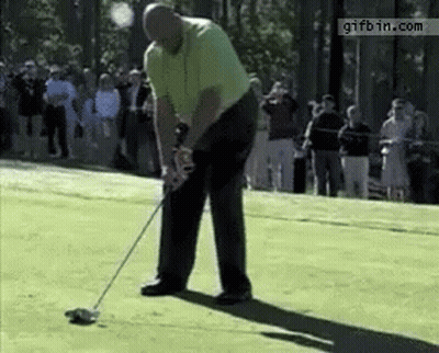 A Man Is Swinging A Golf Club On A Golf Course While A Crowd Watches .. GIF
