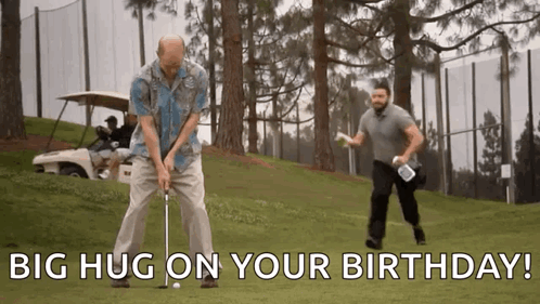 A Man Is Swinging A Golf Club On A Golf Course While Another Man Holds A Golf Bag . GIF