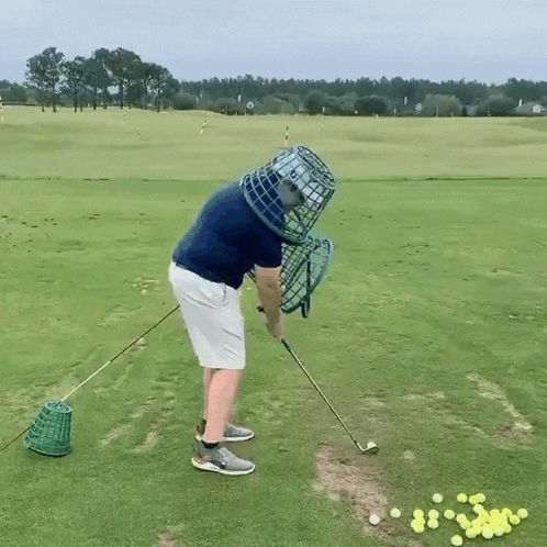 A Man Is Swinging A Golf Club On A Golf Course With A Cage On His Head GIF