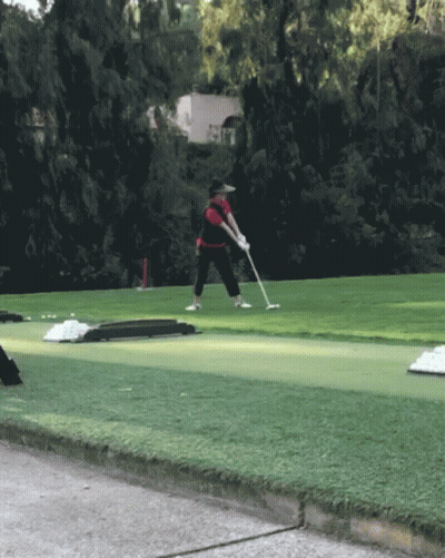 A Man Is Swinging A Golf Club On A Green Course GIF