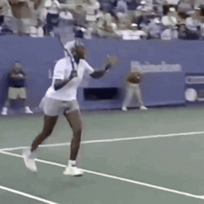 A Man Is Swinging A Tennis Racket On A Tennis Court In Front Of A Crowd . GIF