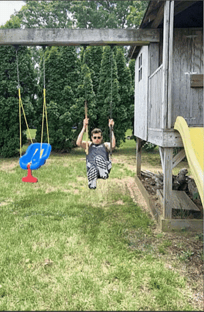 A Man Is Swinging On A Swing Set In A Yard GIF