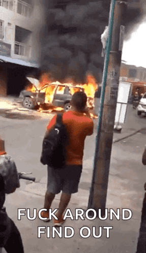 A Man Is Taking A Picture Of A Burning Car With The Words Fuck Around Find Out Written On The Bottom GIF