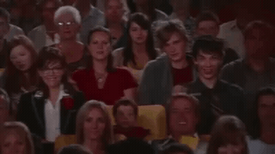 A Man Is Taking A Picture Of A Crowd Of People In A Theatre . GIF