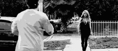 A Man Is Taking A Picture Of A Woman Walking Down The Street . GIF