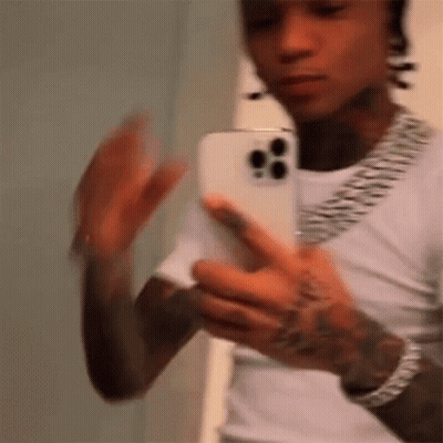 A Man Is Taking A Picture Of Himself In A Mirror With His Phone . GIF
