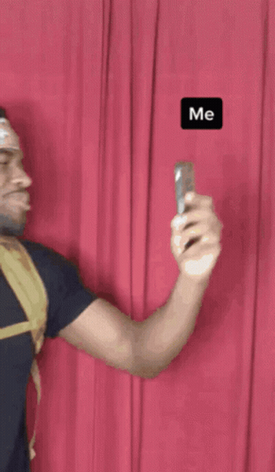 A Man Is Taking A Picture Of Himself With A Red Curtain Behind Him And The Word Me Is On The Bottom Right GIF
