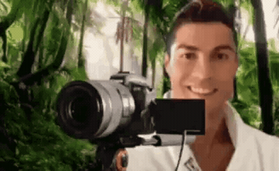 A Man Is Taking A Selfie With A Camera In Front Of A Green Background . GIF