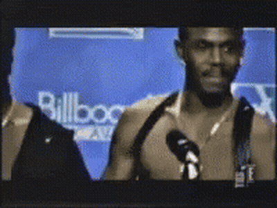 A Man Is Talking Into A Microphone In Front Of A Wall That Says Billboard GIF