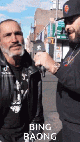A Man Is Talking Into A Microphone While Another Man Looks On And Says Bing Baong GIF