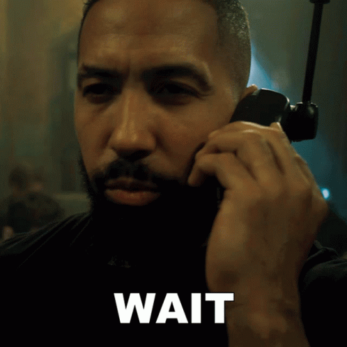 A Man Is Talking On A Cell Phone And The Word Wait Is Below Him GIF