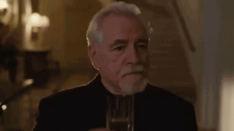 A Man Is Talking On A Cell Phone In A Room With A Chandelier In The Background . GIF