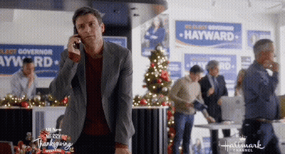 A Man Is Talking On A Cell Phone In Front Of A Hallmark Channel Ad For Hayward . GIF