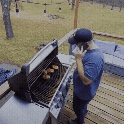 A Man Is Talking On A Cell Phone While Grilling GIF