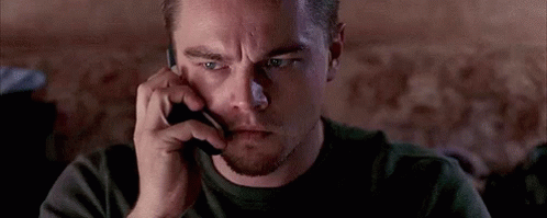 A Man Is Talking On A Cell Phone While Looking At Something . GIF