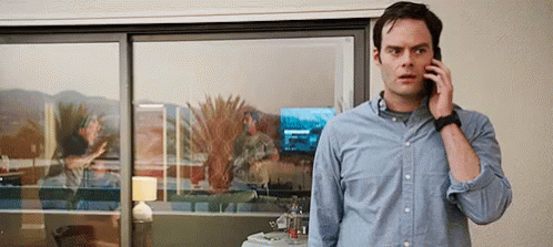A Man Is Talking On A Cell Phone While Standing In Front Of A Sliding Glass Door . GIF