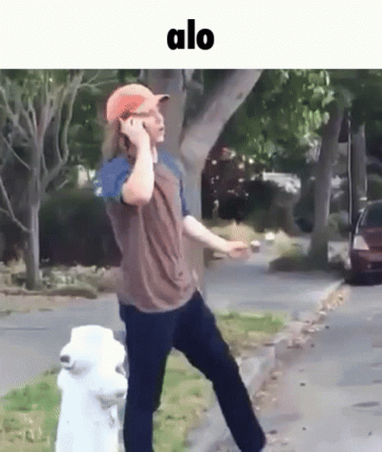 A Man Is Talking On A Cell Phone While Standing Next To A White Fire Hydrant . GIF