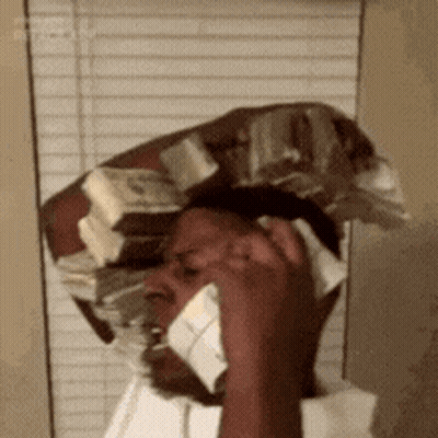 A Man Is Talking On A Cell Phone While Wearing A Hat Made Of Money . GIF