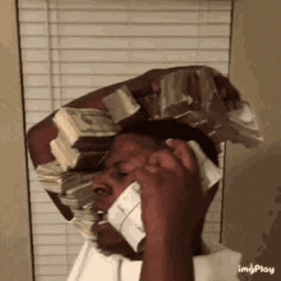 A Man Is Talking On A Cell Phone While Wearing A Stack Of Money On His Head . GIF