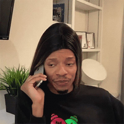 A Man Is Talking On A Cell Phone While Wearing A Wig . GIF