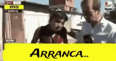 A Man Is Talking On A Cell Phone With A Yellow Sign That Says Arranca . GIF