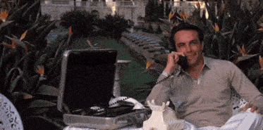 A Man Is Talking On A Phone In Front Of A Briefcase GIF