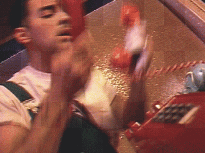 A Man Is Talking On A Red Telephone With His Hand Up GIF