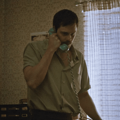 A Man Is Talking On A Telephone In Front Of A Window GIF