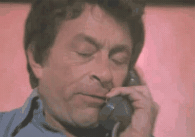 A Man Is Talking On A Telephone With His Eyes Closed And His Mouth Open . GIF