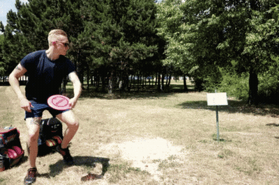 A Man Is Throwing A Frisbee In A Field With Trees In The Background And A Sign That Says " A " GIF