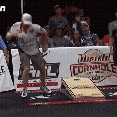 A Man Is Throwing A Frisbee In Front Of A Johnsonville Cornhole Sign GIF