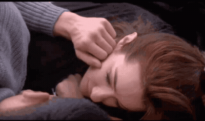 A Man Is Touching A Woman 'S Face While Laying On A Bed GIF